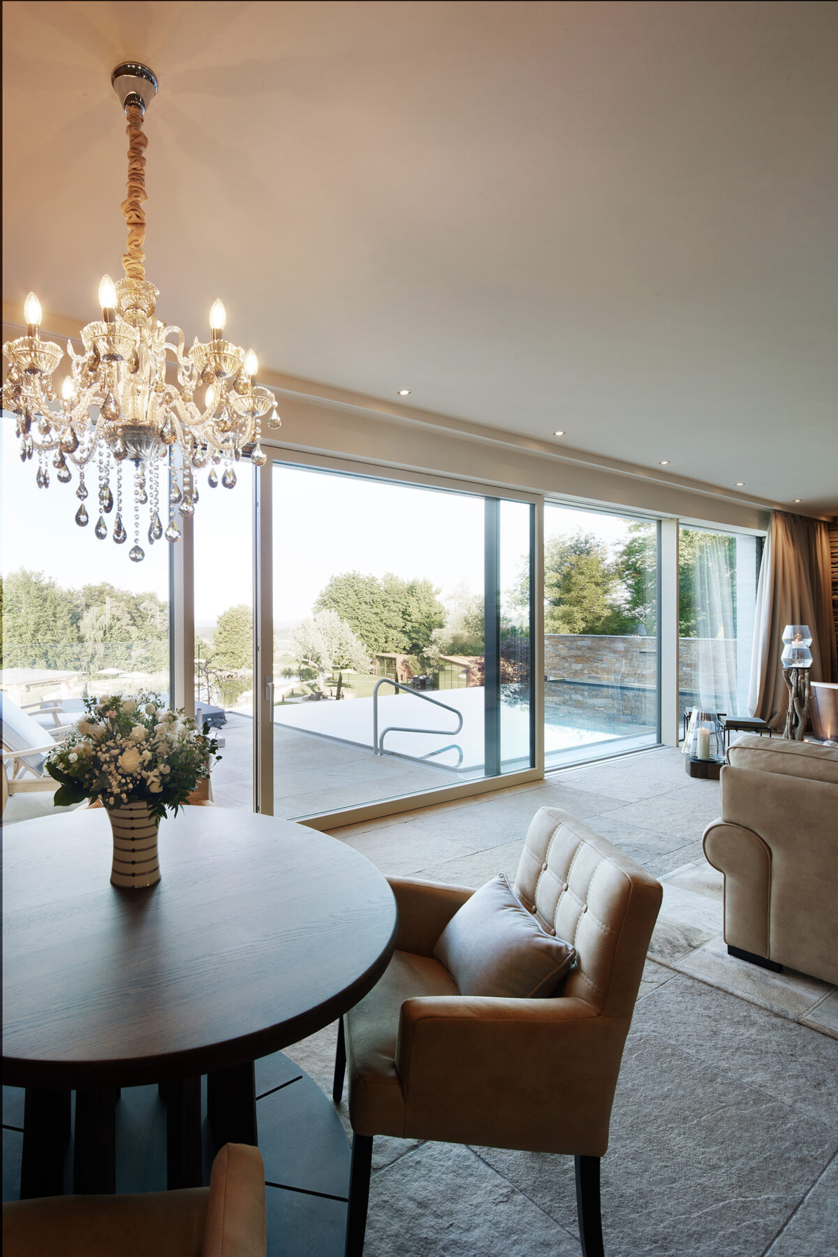 Architekturfotografie eines eleganten Essbereichs mit Kristallleuchter und Hebeschiebetüren von Gaulhofer im Golden Hill Resort.