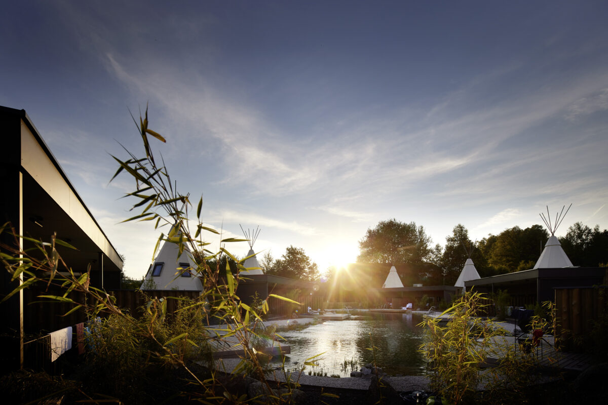 Architekturfotografie des IKUNA Naturresorts in Natternbach bei Sonnenuntergang mit Tipi-Suiten am See.