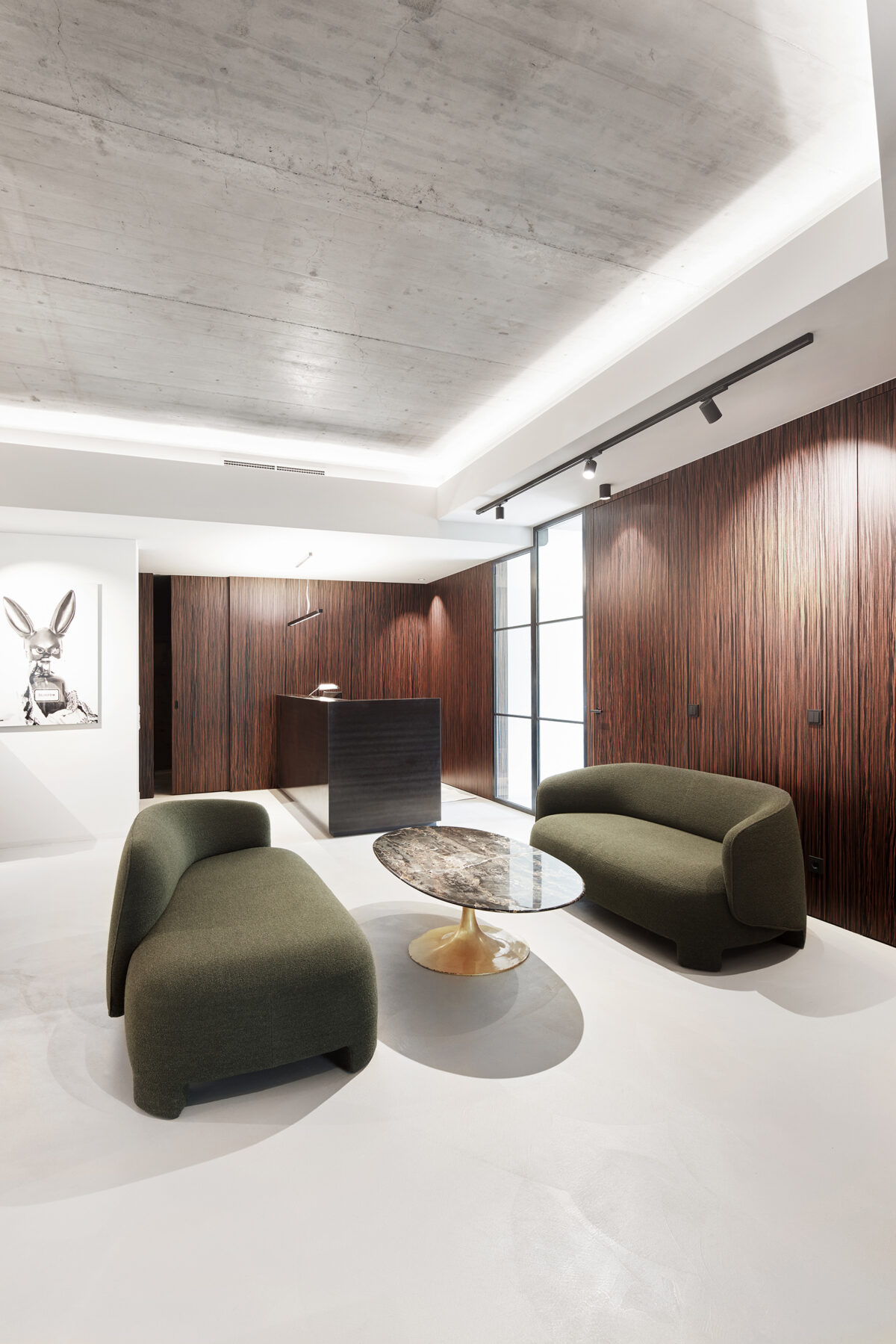 Stilvolle Kanzlei-Lobby in Vorarlberg mit moosgrünen Design-Sofas, Sichtbetondecke und Holzverkleidung von Gahleitner Architekten.