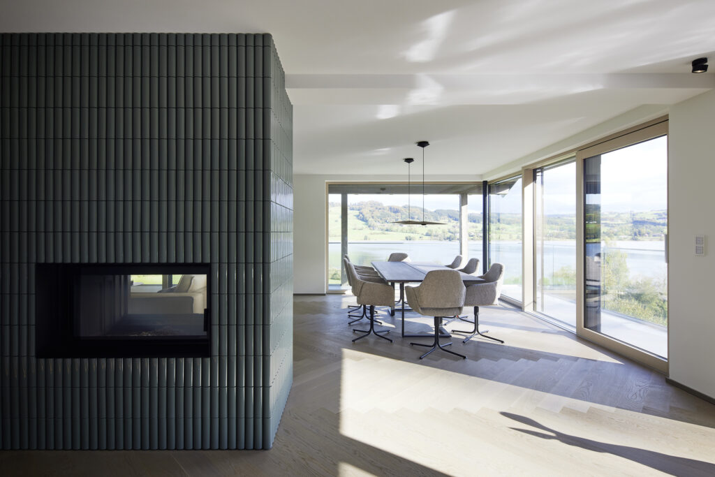 Moderner Essbereich und Kachelofen im Haus am Irrsee mit großflächigen Panoramafenstern und direktem Seeblick, geplant von Martina Hirschber