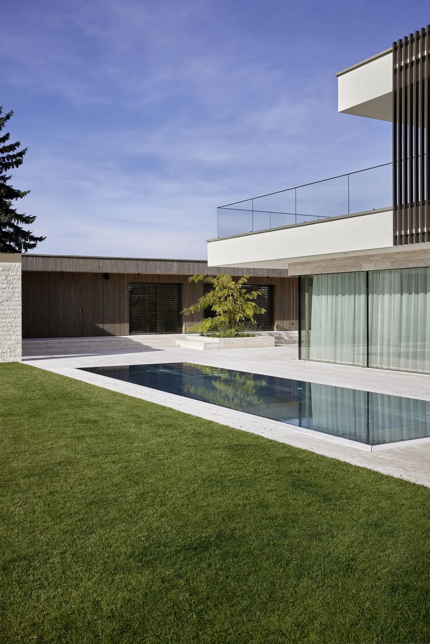 Moderne Luxusvilla in Steyr bei Tageslicht mit einer gepflegten Rasenfläche, Steinterrasse und eingebautem Außenpool, geplant von Architekt Michael Obermair, professionelle Architekturfotografie von Roland Wimmer.