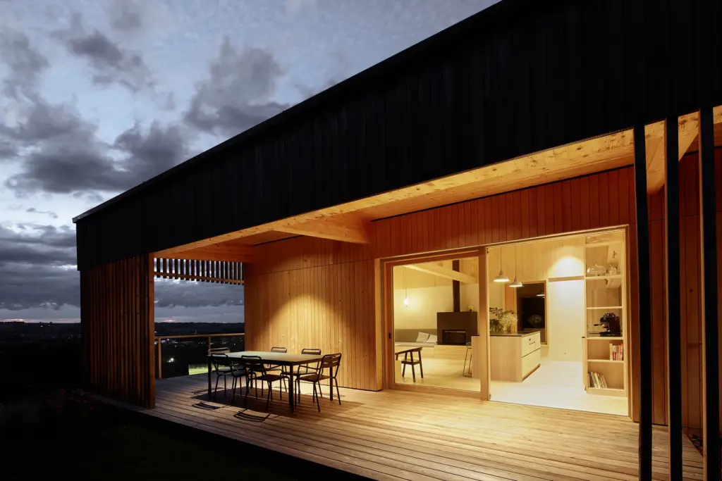 Modernes Holzhaus bei Nacht mit überdachter Terrasse und Hebeschiebetür, geplant von Kontur Architekten mit Fenstern von Palisa Bauelemente 