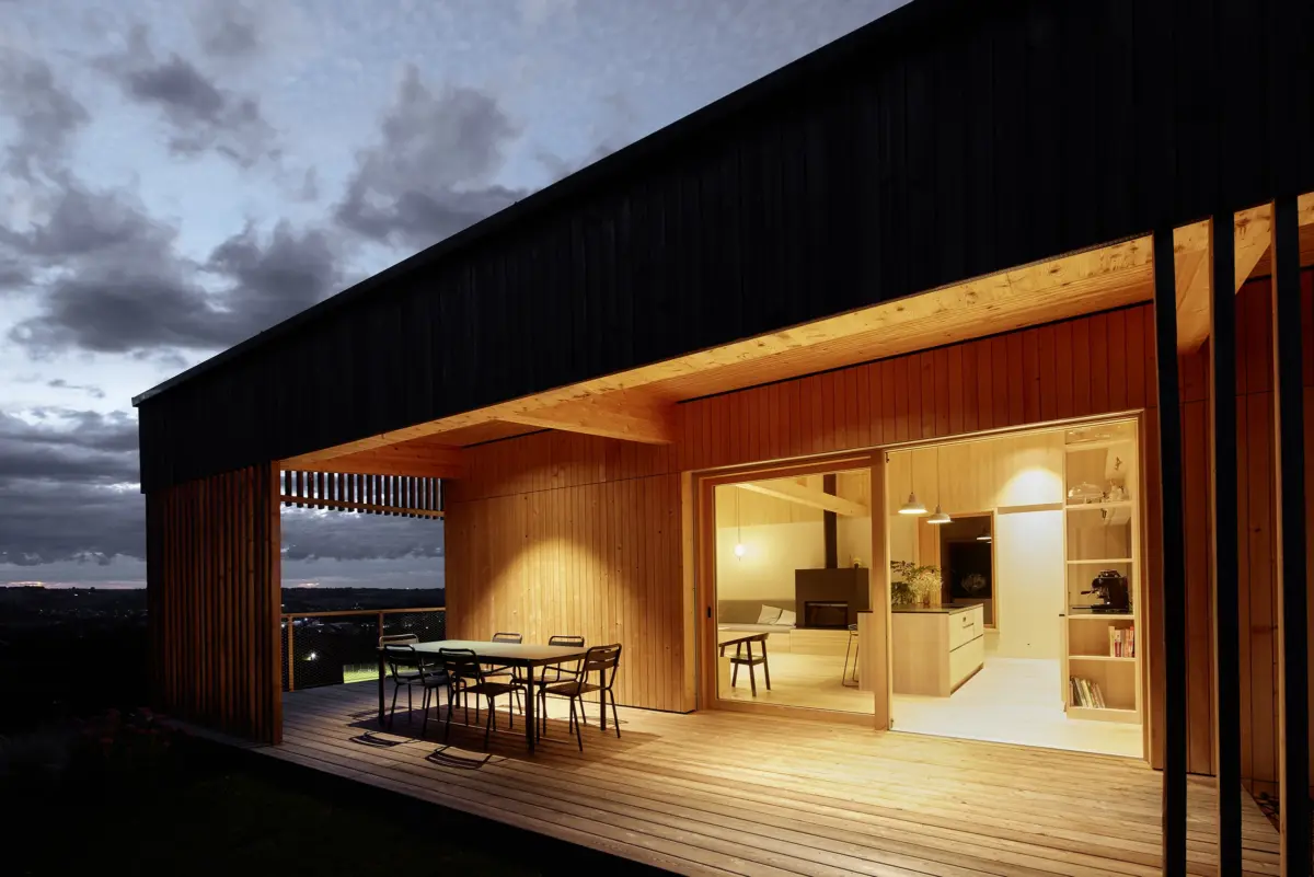Modernes Holzhaus bei Nacht mit überdachter Terrasse und Hebeschiebetür, geplant von Kontur Architekten mit Fenstern von Palisa Bauelemente und Böhler Fenster, Architekturfotografie von Roland Wimmer.