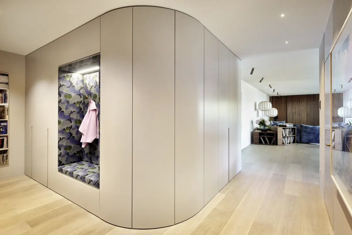 Garderobe mit geschwungener Einbauschrankwand und Sitznische mit Ginkgo-Tapete, dahinter der Wohnraum einer Wohnung in Bregenz von Gahleitner Architekten