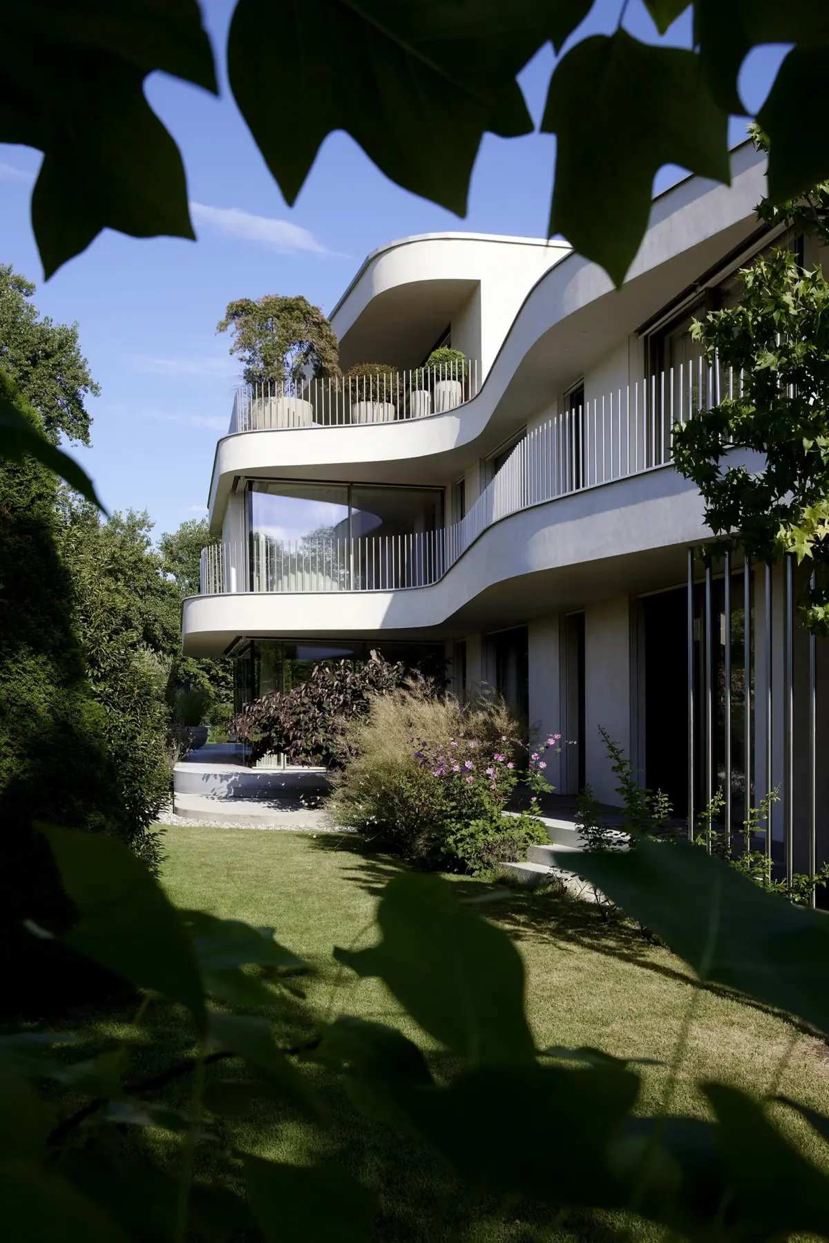 Geschwungene Fassade durch Blätter fotografiert, Hochformat einer Villa am Bodensee bei Bregenz, Gahleitner Architekten, Architekturfotograf Roland Wimmer