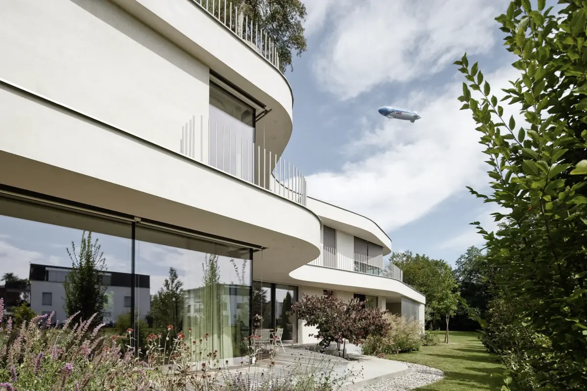 Geschwungene weiße Fassade mit Glasfront, im Himmel ein Zeppelin über dem Bodensee, Villa Villa am Bodensee bei Bregenz, Gahleitner Architekten, Architekturfotograf Roland Wimmer